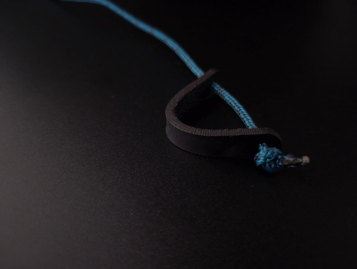 A close-up of a black leather loop with a bright blue braided cord threaded through it, photographed on a dark black background.