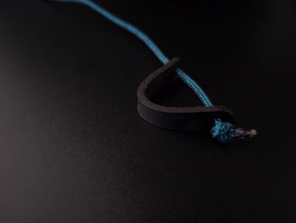 A close-up of a black leather loop with a bright blue braided cord threaded through it, photographed on a dark black background.