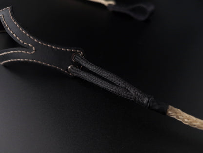 Close-up of a black shepherd sling with light tan contrast stitching and a braided black-and-tan cord, shown on a dark background.