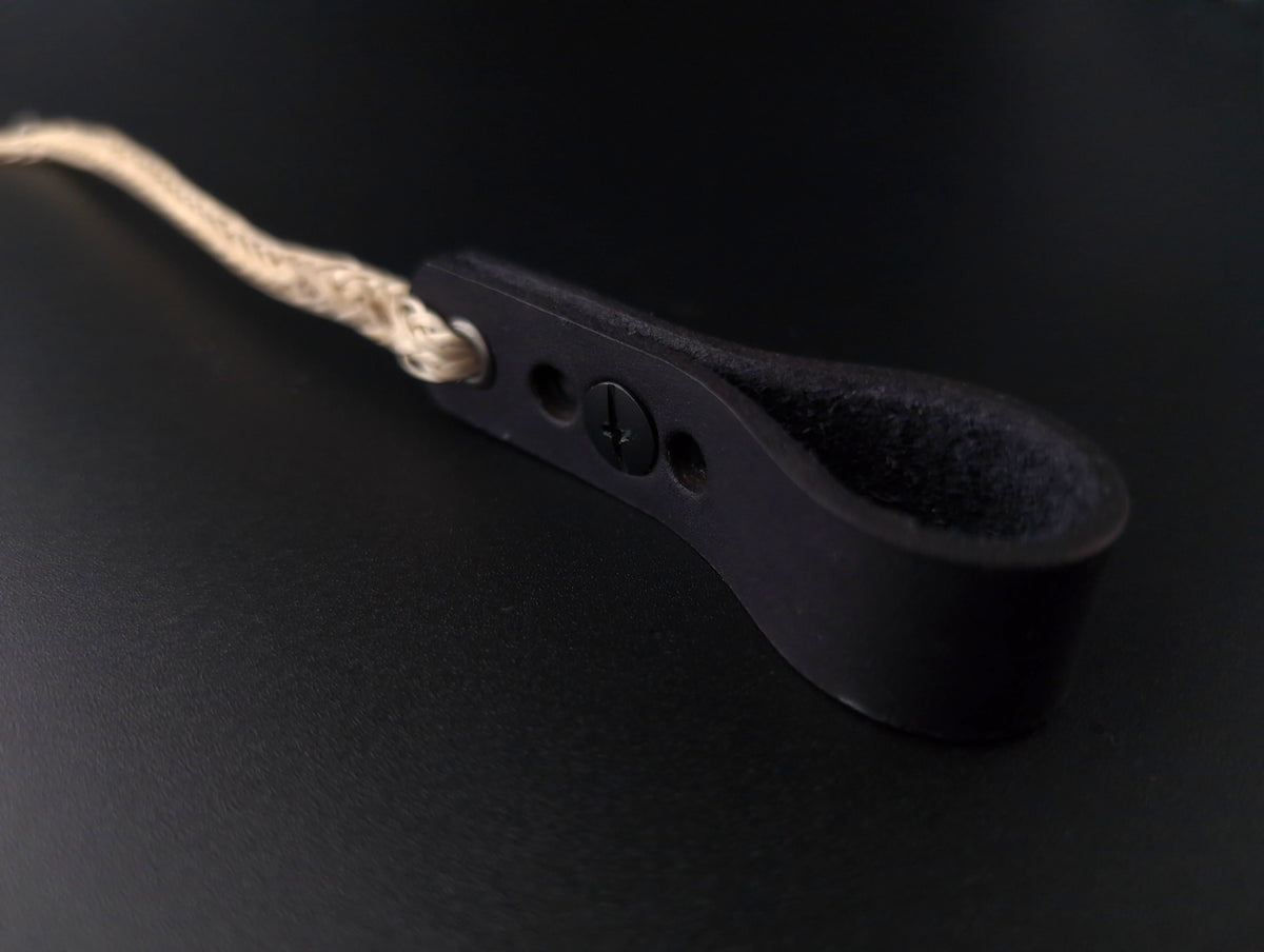 A close-up of a black leather strap with a looped end, a small screw detail, and a beige braided cord attached, set against a dark background.