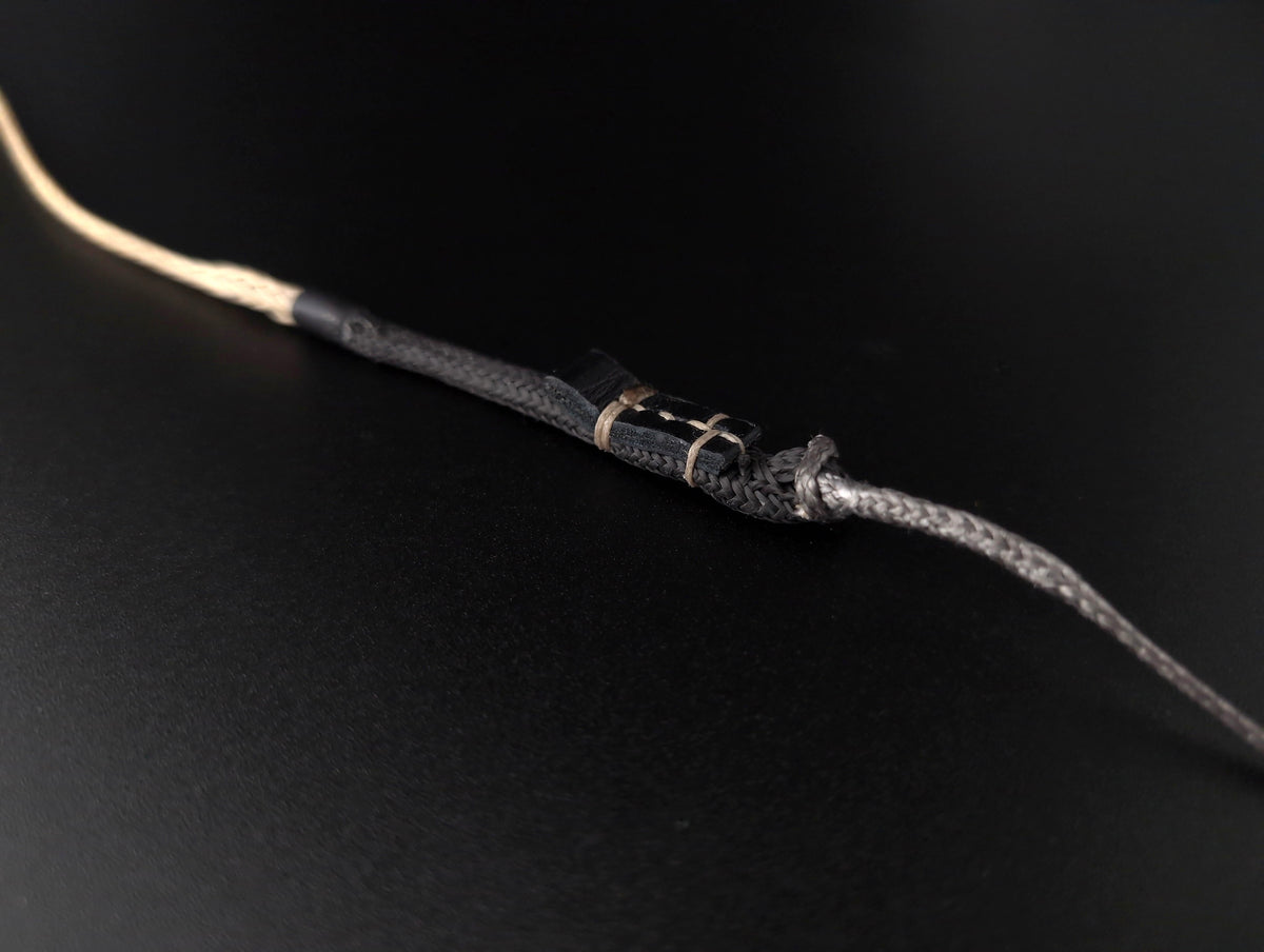 A close-up of a braidedbeige vectran cord with black dyneema sheathing and a leather tab hand stitched on
